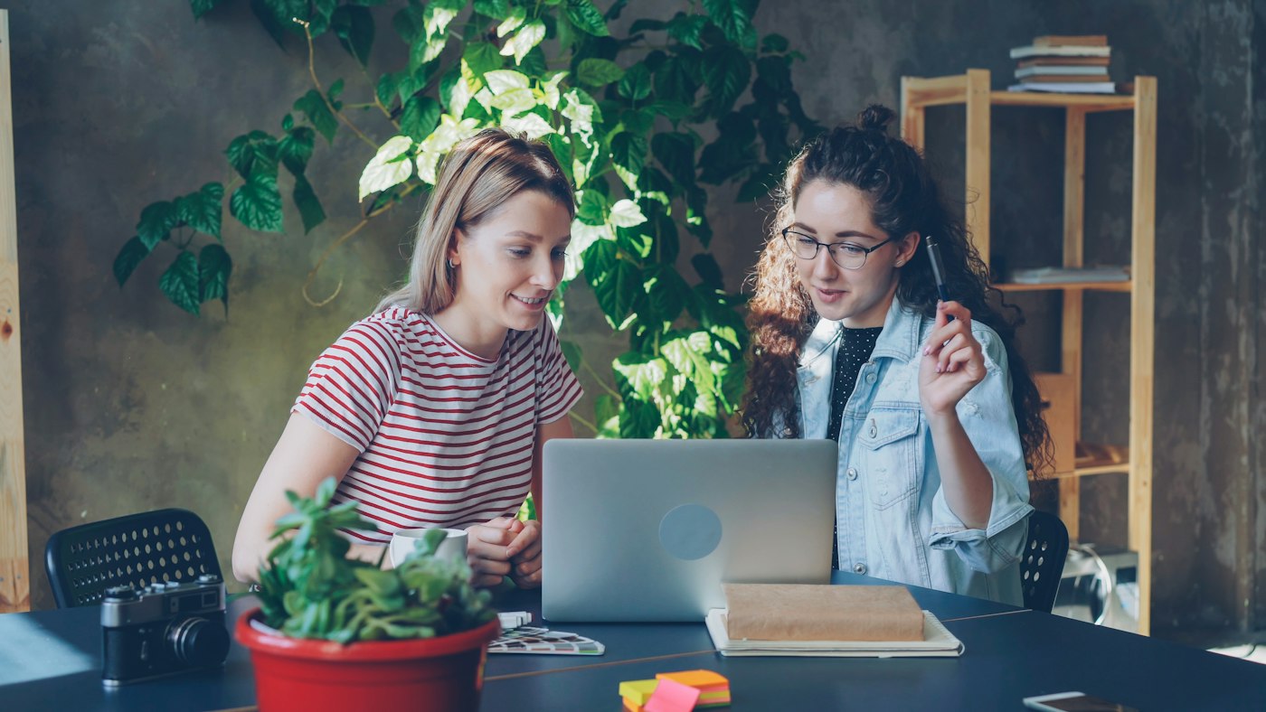Two colleagues working together at a laptop among office plants